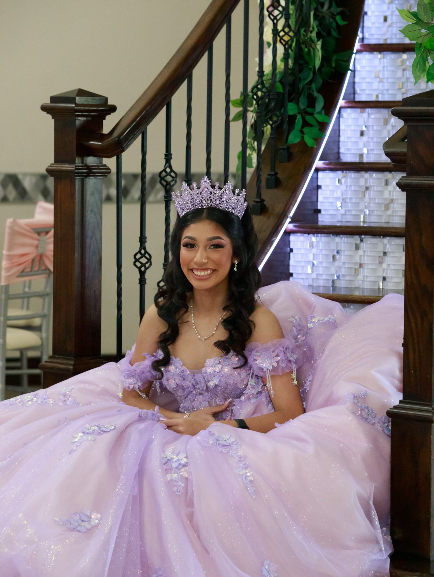 Young woman in a lavender quinceanera dress with jeweled details poses elegantly on a staircase.