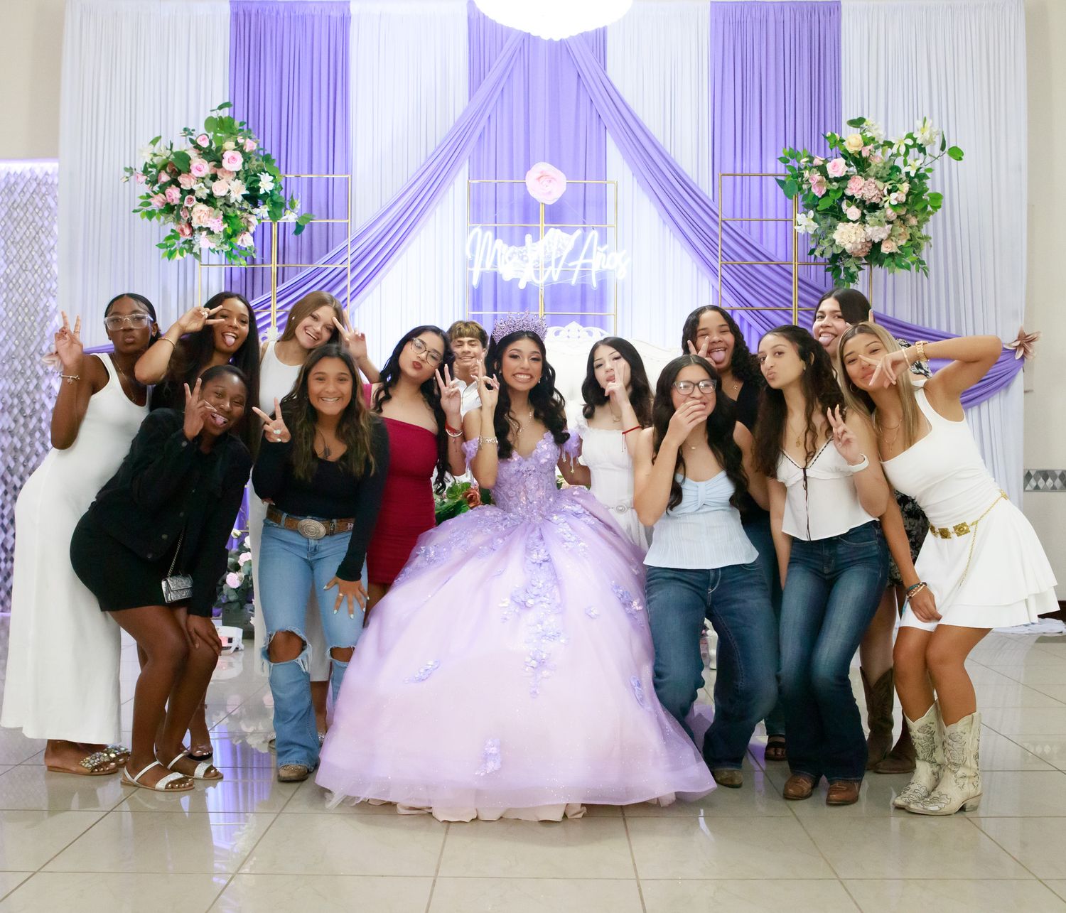 A group of people pose together in a white ballroom decorated with purple lighting and floral arrangements.