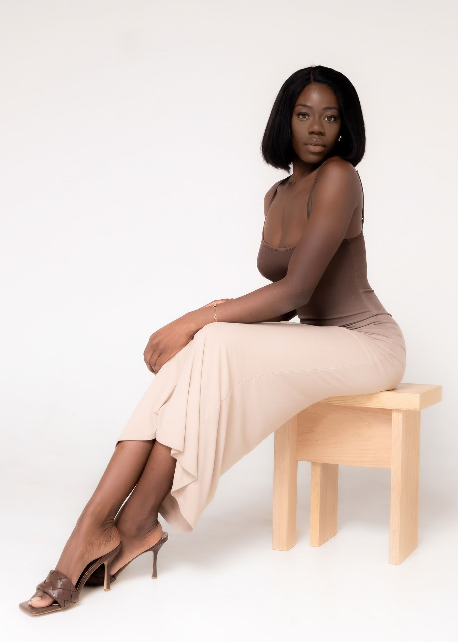 Woman seated on a wooden stool for a self-portrait against a light studio background.