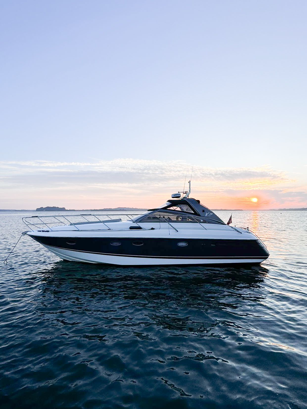 Luxury sports yacht cruising on calm ocean waters during a spectacular golden sunset against the horizon.