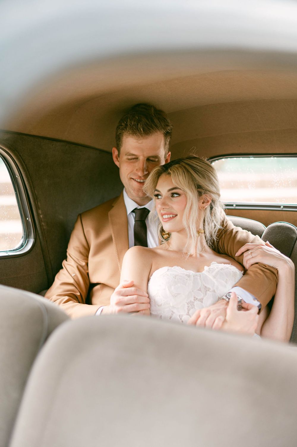 A romantic moment between newlyweds in the back seat of a classic car during their wedding photoshoot.