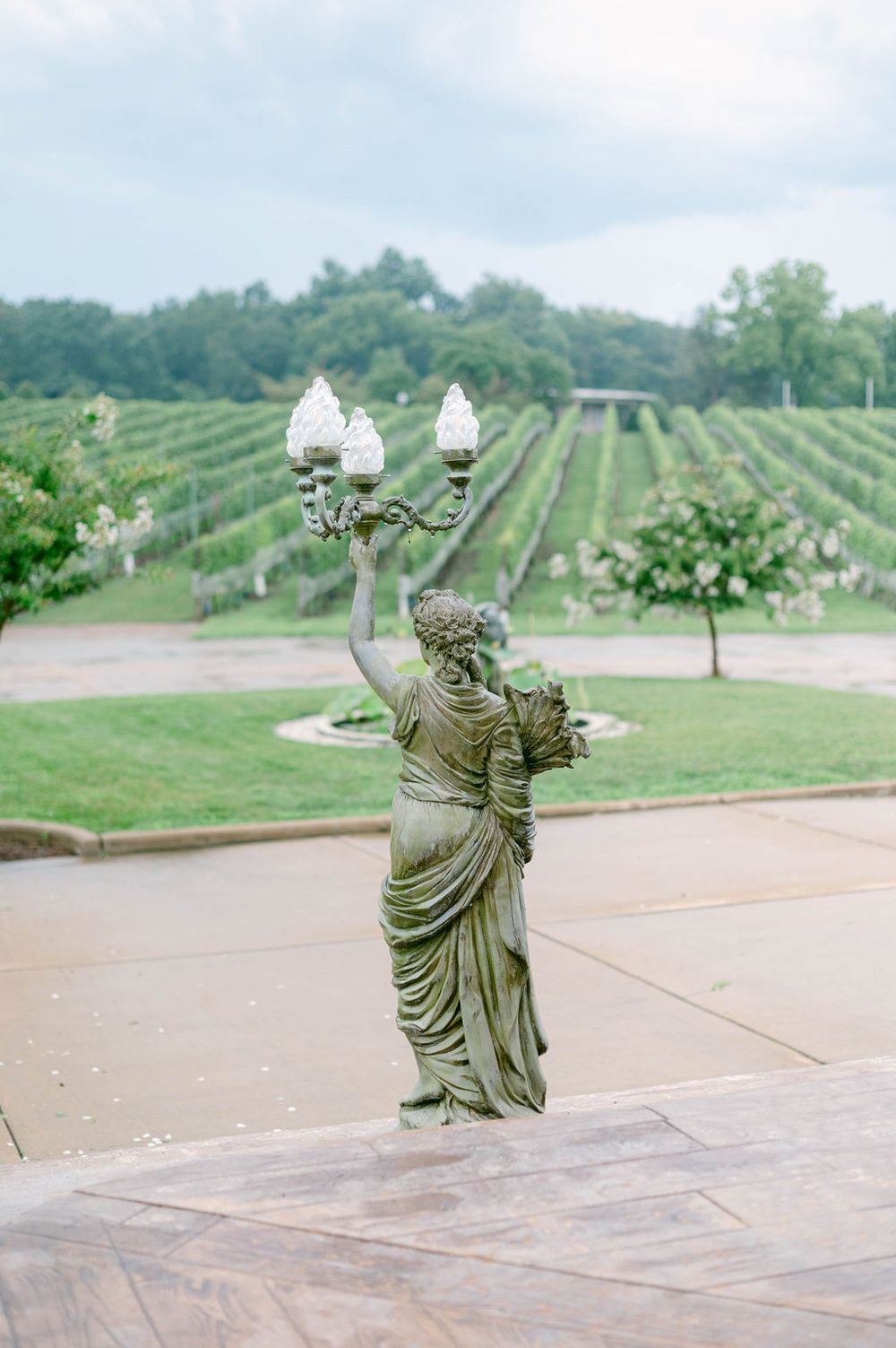 Bronze statues in flowing robes appear to be dancing across a plaza with green vineyards rolling in the background at Morais Vineyards.