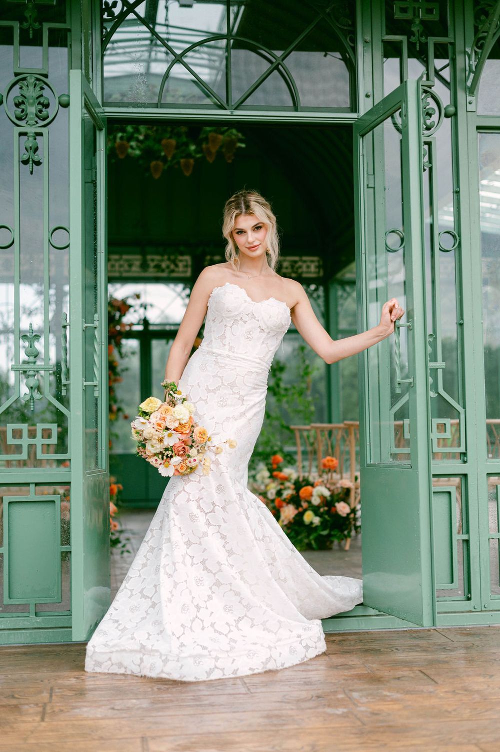 A stunning mermaid-style wedding dress with lace details photographed in front of vintage green doors at an elegant venue.