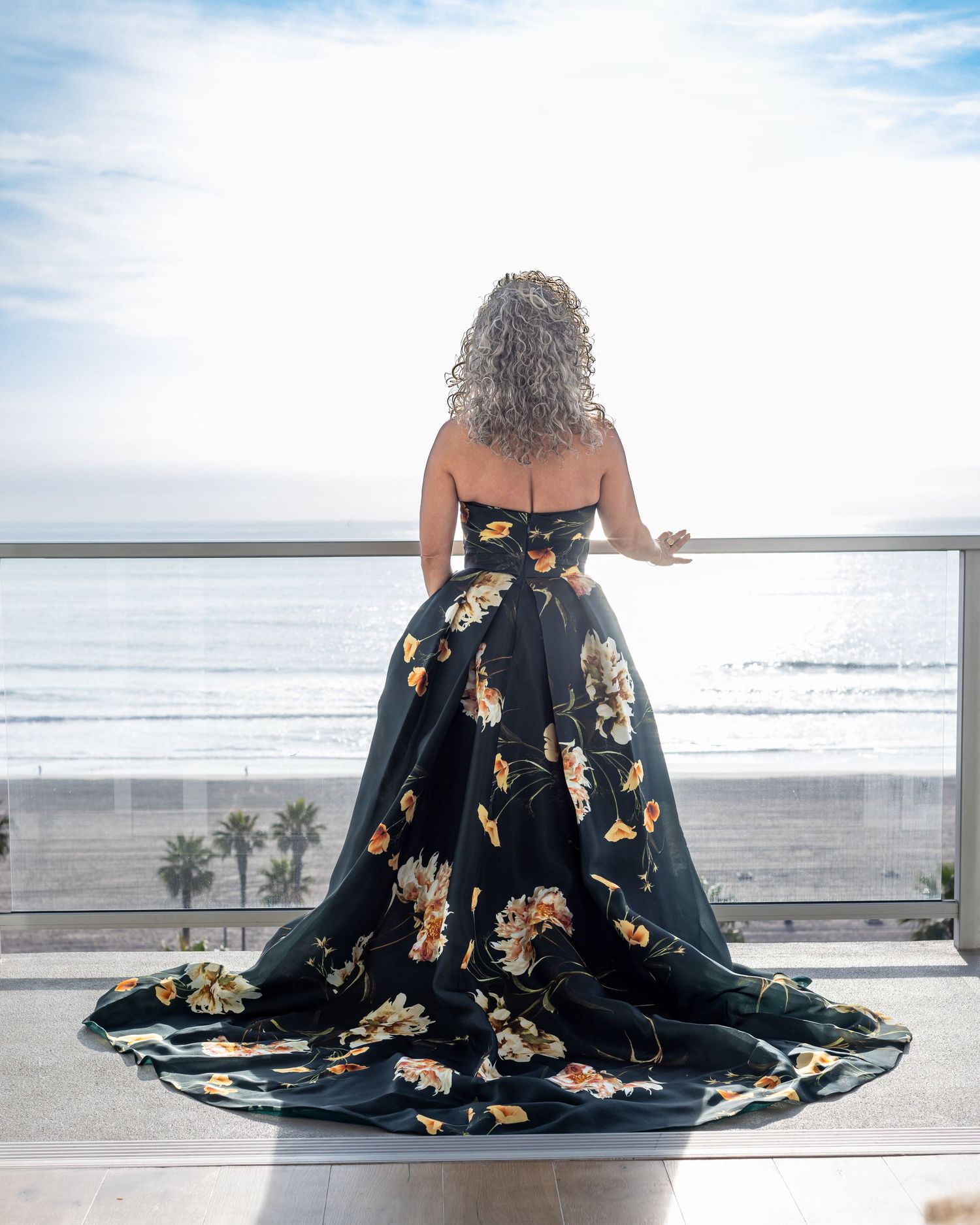 A flowing green flower print wedding dress gown with gold butterfly patterns photographed at the beach during sunset.