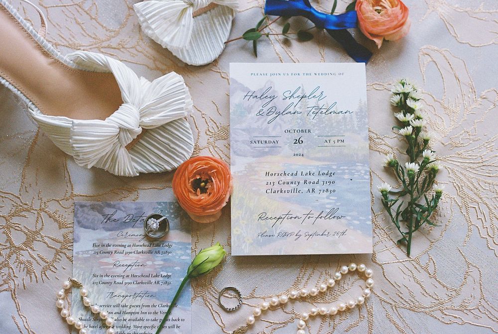 Wedding details flatlay with invitation cards, rings, flowers and delicate pearl accessories on lace background.