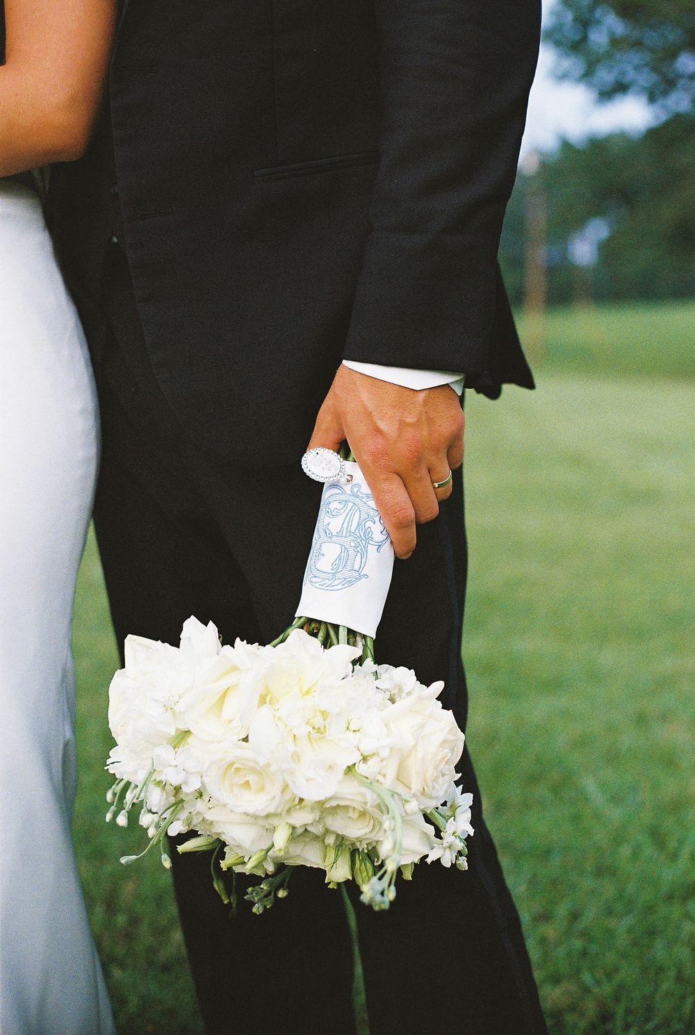 A wedding detail photo showing hands holding white floral bouquets against formal black attire.