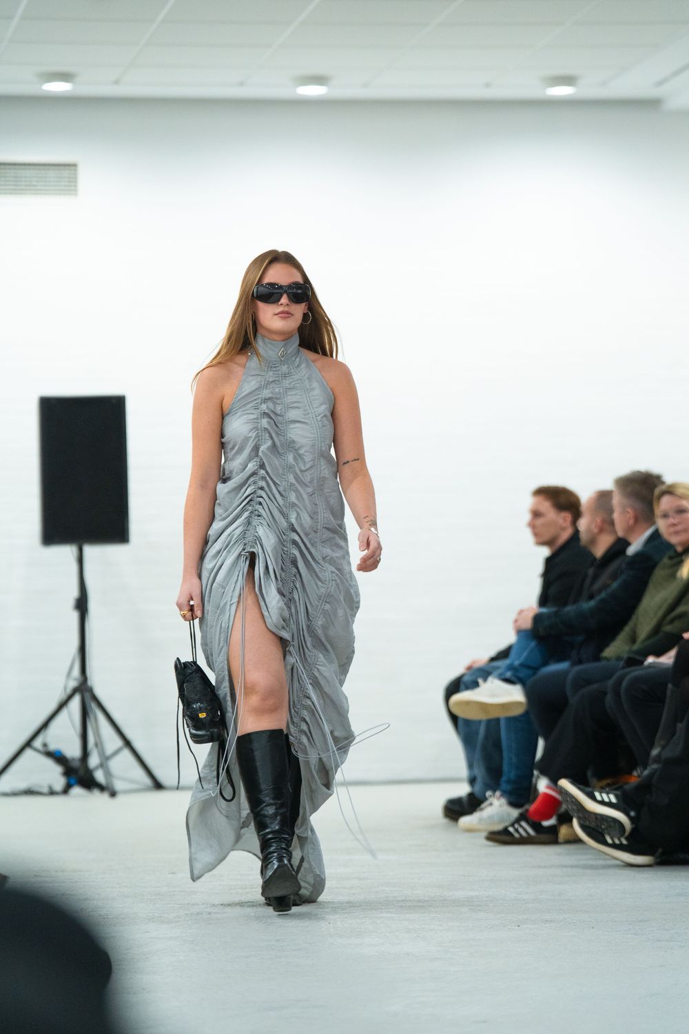 Fashion runway show with model in draped gray dress and boots.
