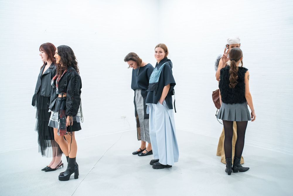 Fashion show lineup with models in monochromatic outfits against white backdrop.