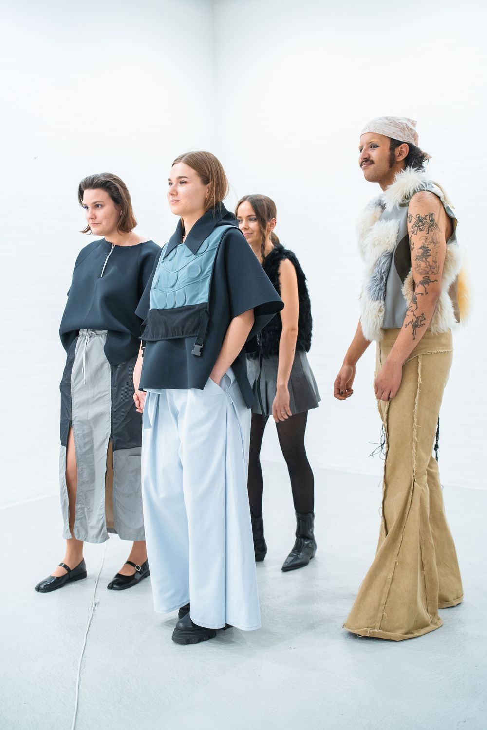 Models lined up wearing minimalist apron-style dresses in white, gray and tan.