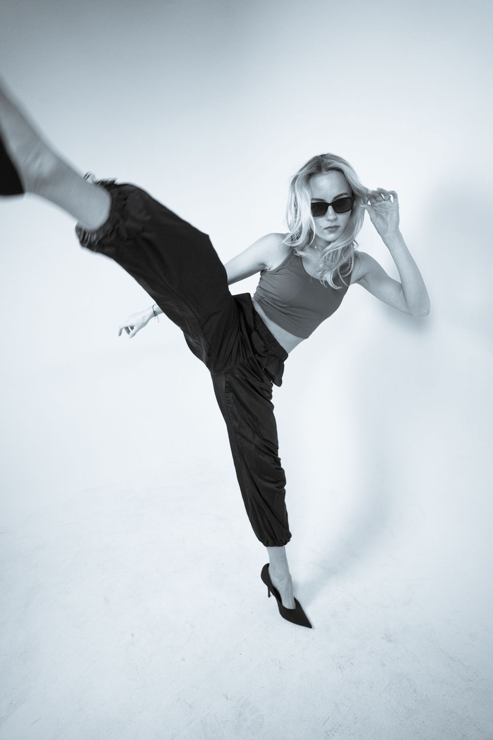 Dancer performing high kicks in black outfit against white background.