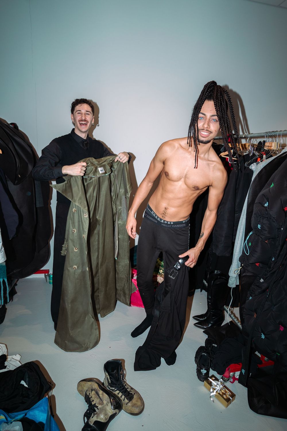 Backstage fashion show scene with clothing racks and casual military-style jackets.