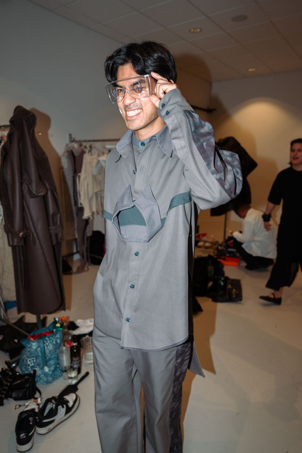 Behind-the-scenes fitting room showing models in gray formal wear and suits.