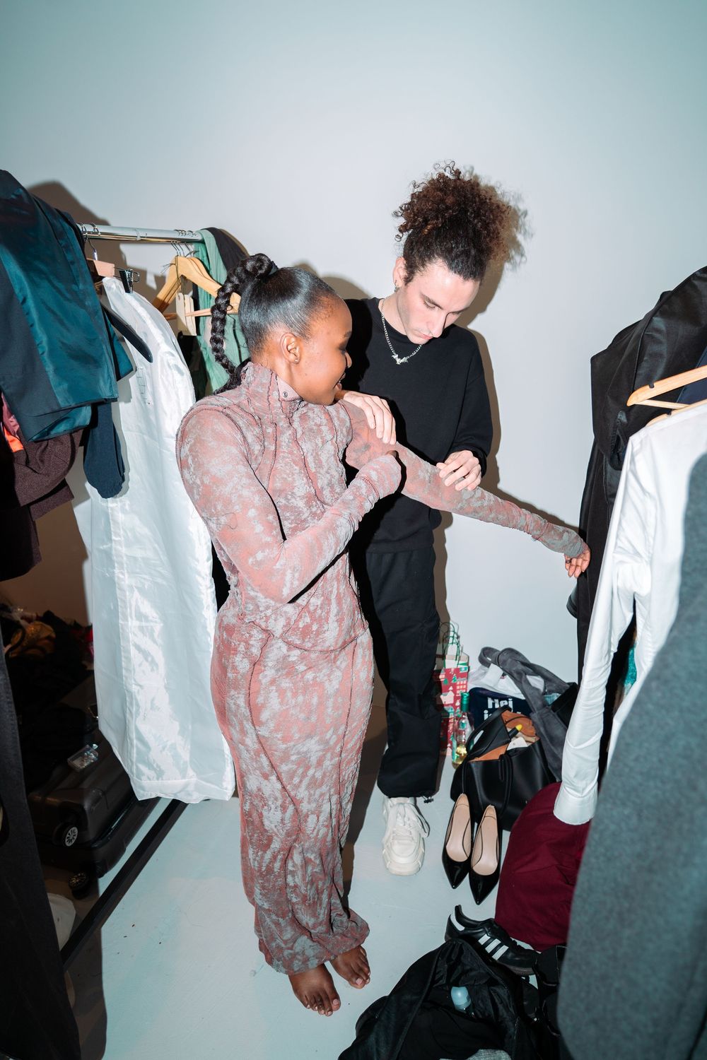 Models preparing backstage wearing floral and dark colored outfits.
