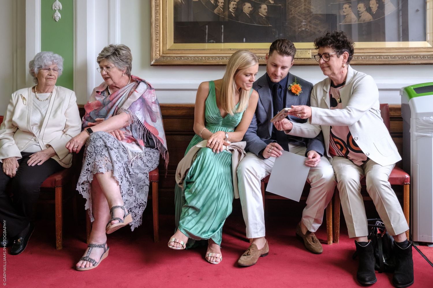 Wedding guests relaxing and chatting while seated along a wall.