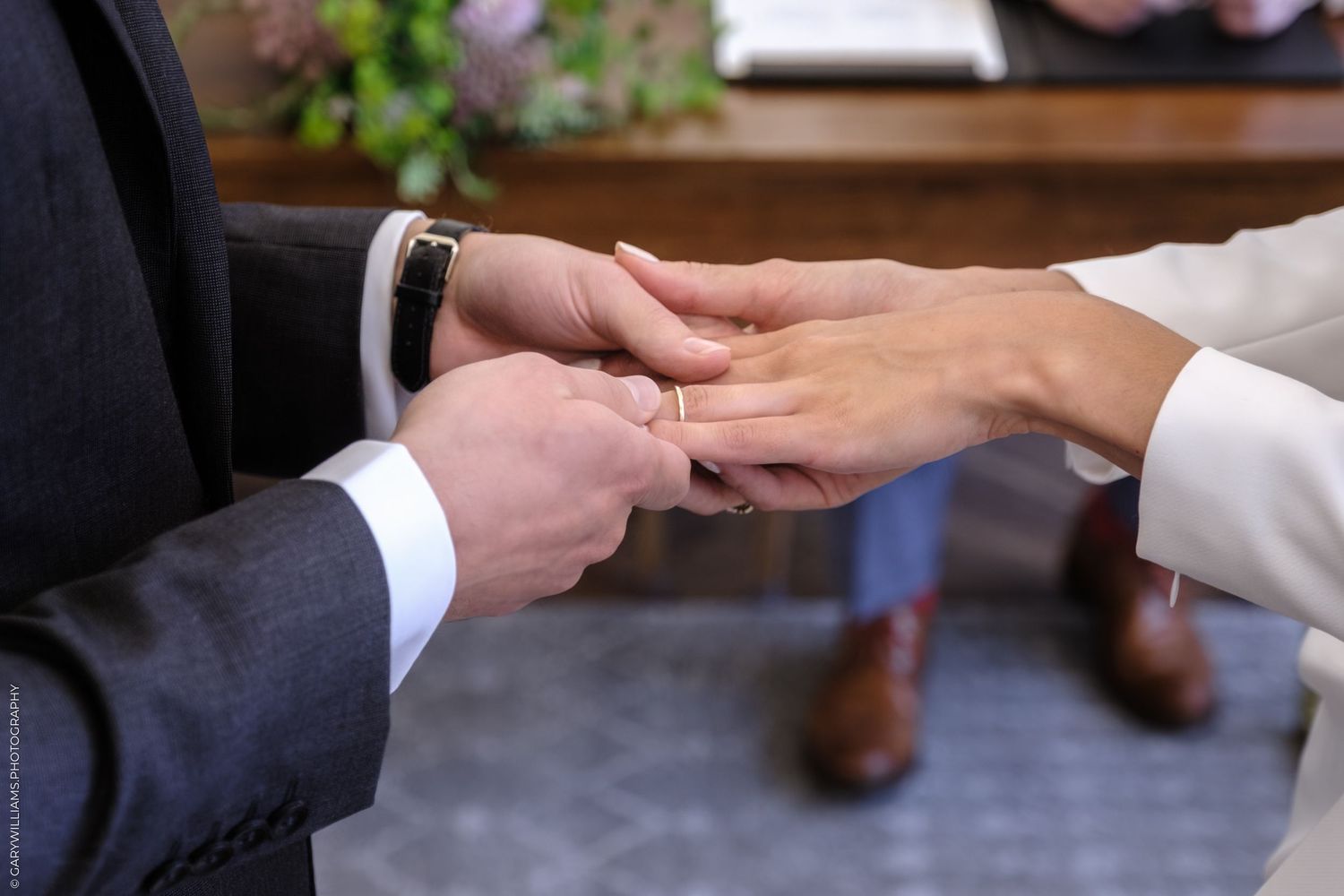 Close-up view of hands exchanging wedding rings during a traditional marriage ceremony in formal attire.