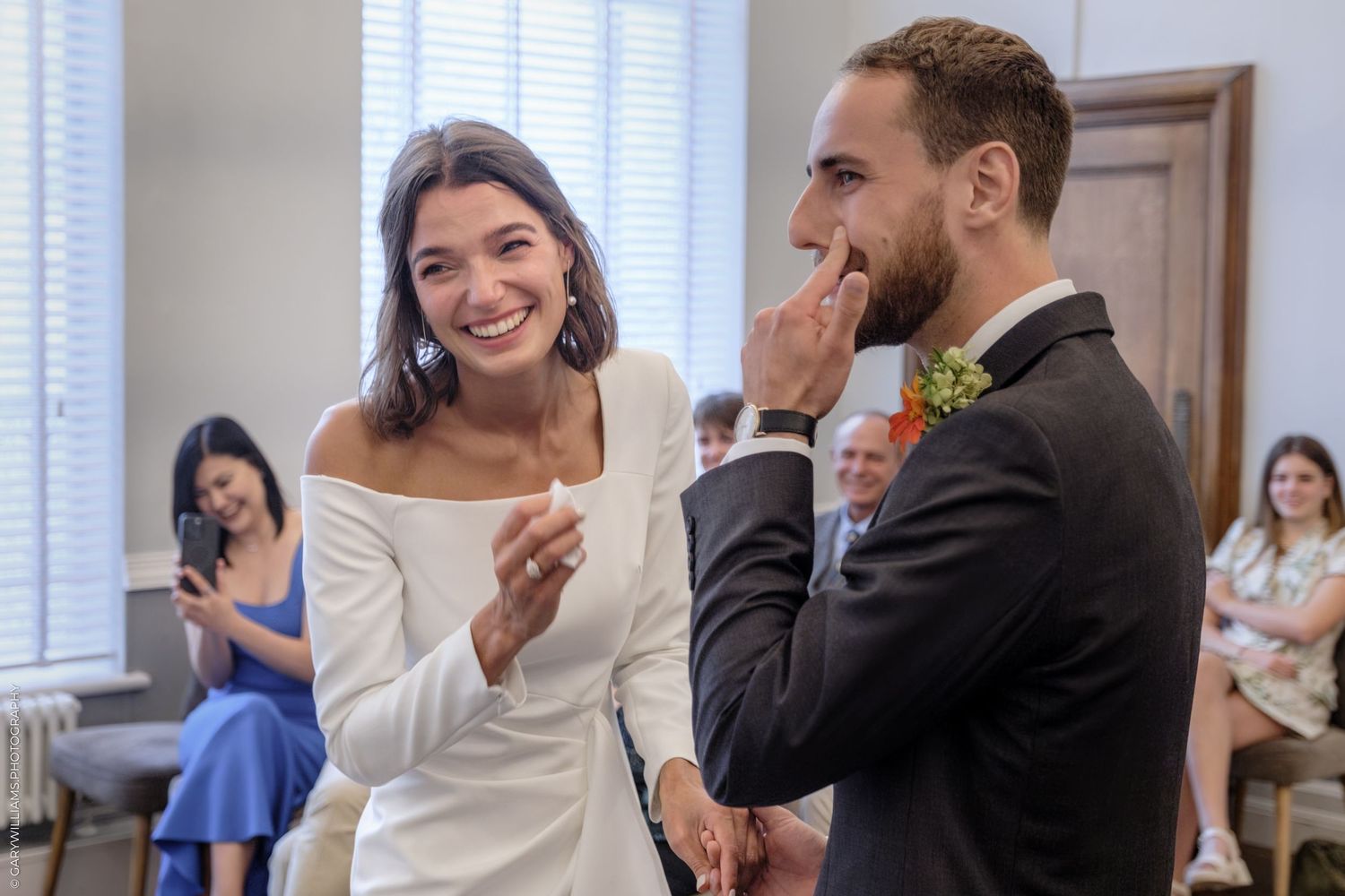A couple shares a kiss during a wedding ceremony as wedding guests look on and smile.
