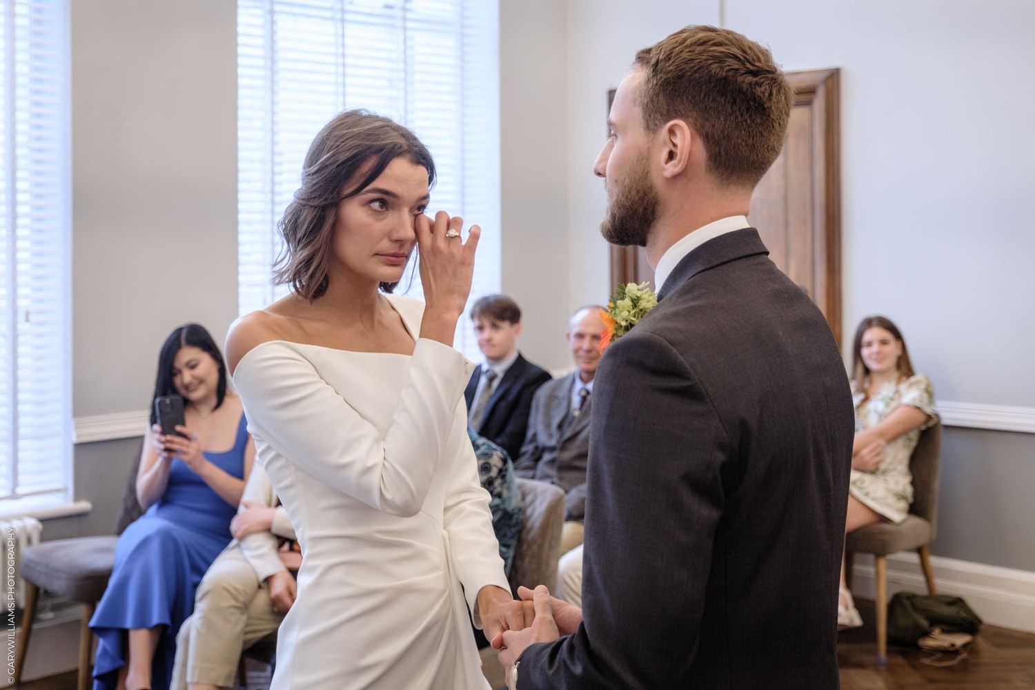 A bride and groom share an emotional moment during their wedding ceremony in a bright indoor venue.
