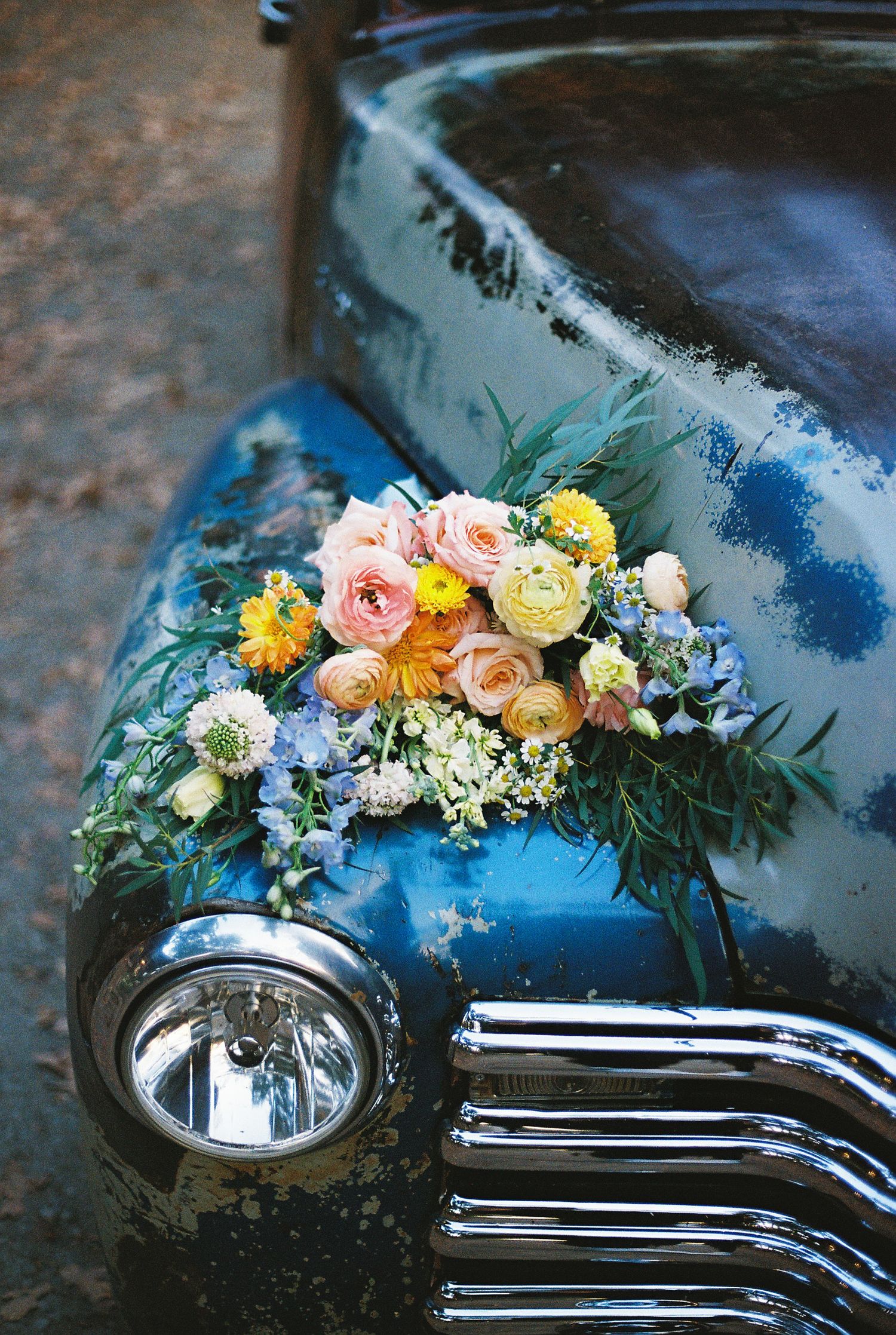 Vintage blue car decorated with pastel floral arrangements for a wedding.