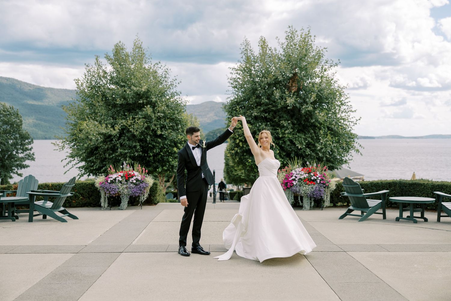 Wedding party enjoys a joyful moment on a green boardwalk overlooking a scenic coastal view with summer trees.