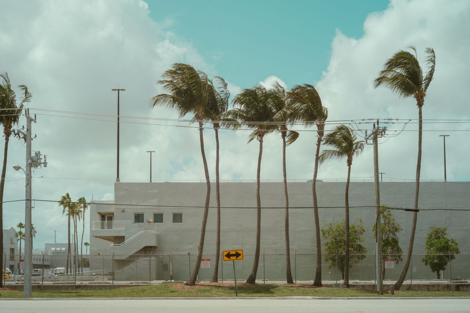Multiple cargo shipping containers stacked in an industrial yard under a cloudy blue sky.