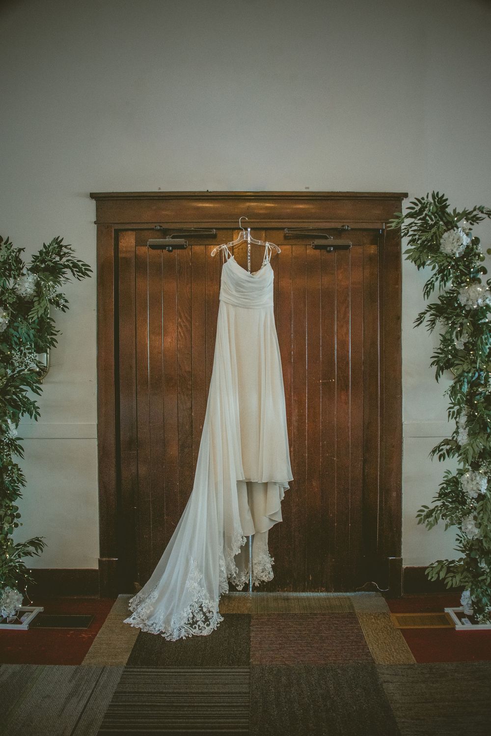 A sequence of white wedding dresses hanging on rustic wooden walls with greenery decorations.