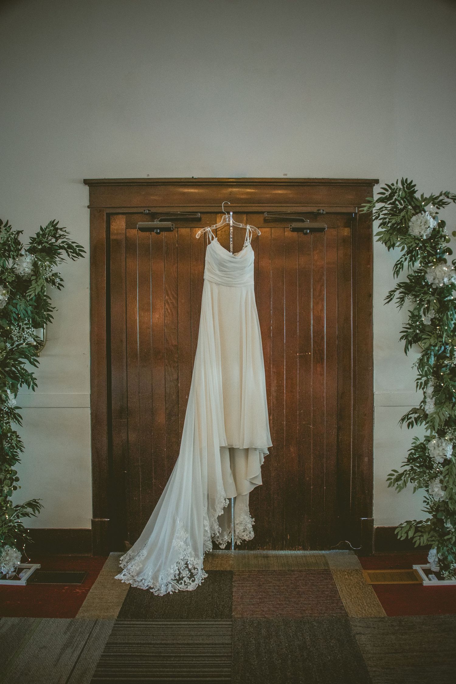 A sequence of white wedding dresses hanging on rustic wooden walls with greenery decorations.