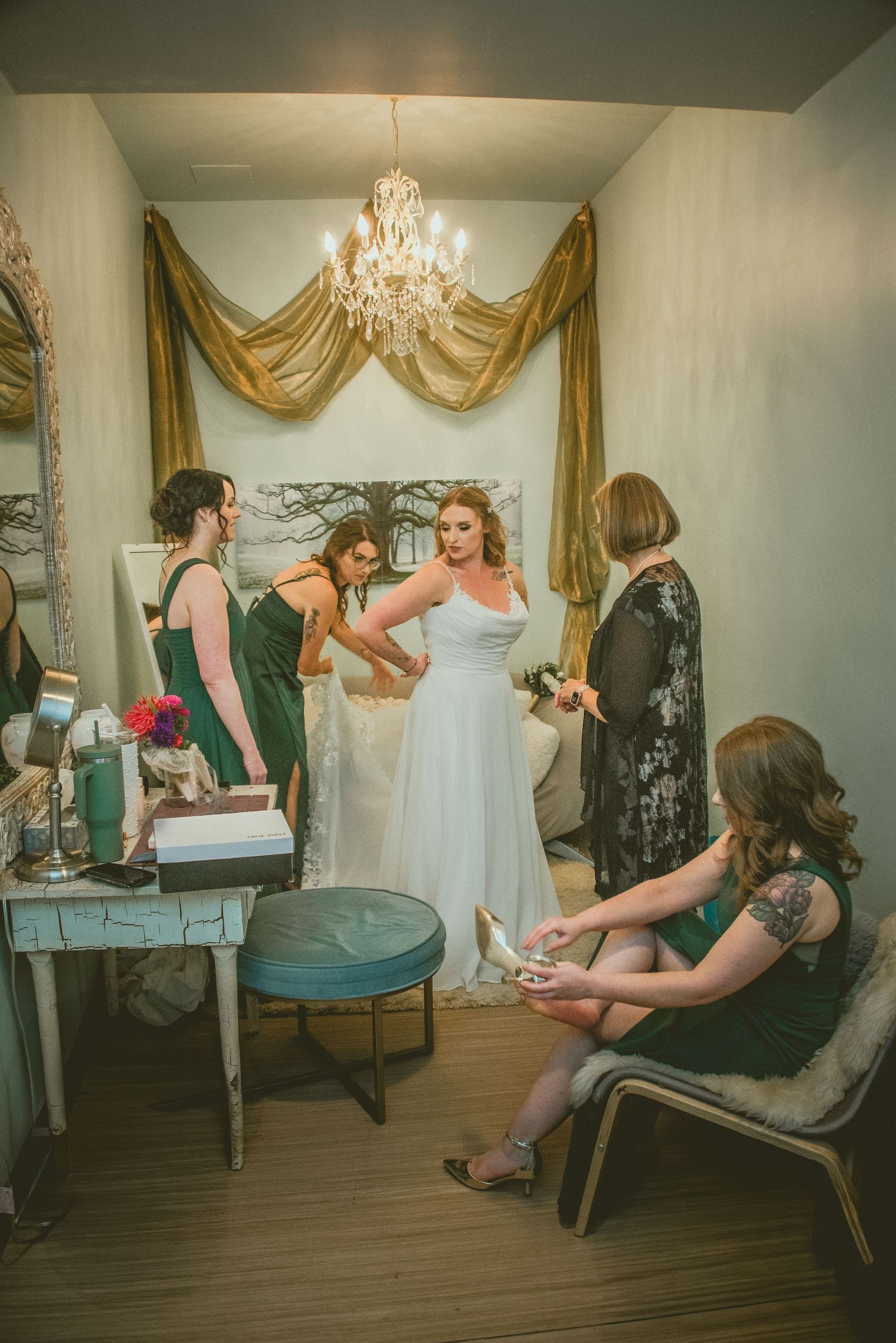 Wedding party members relax and get ready in an elegant dressing room with gold curtains and a chandelier.