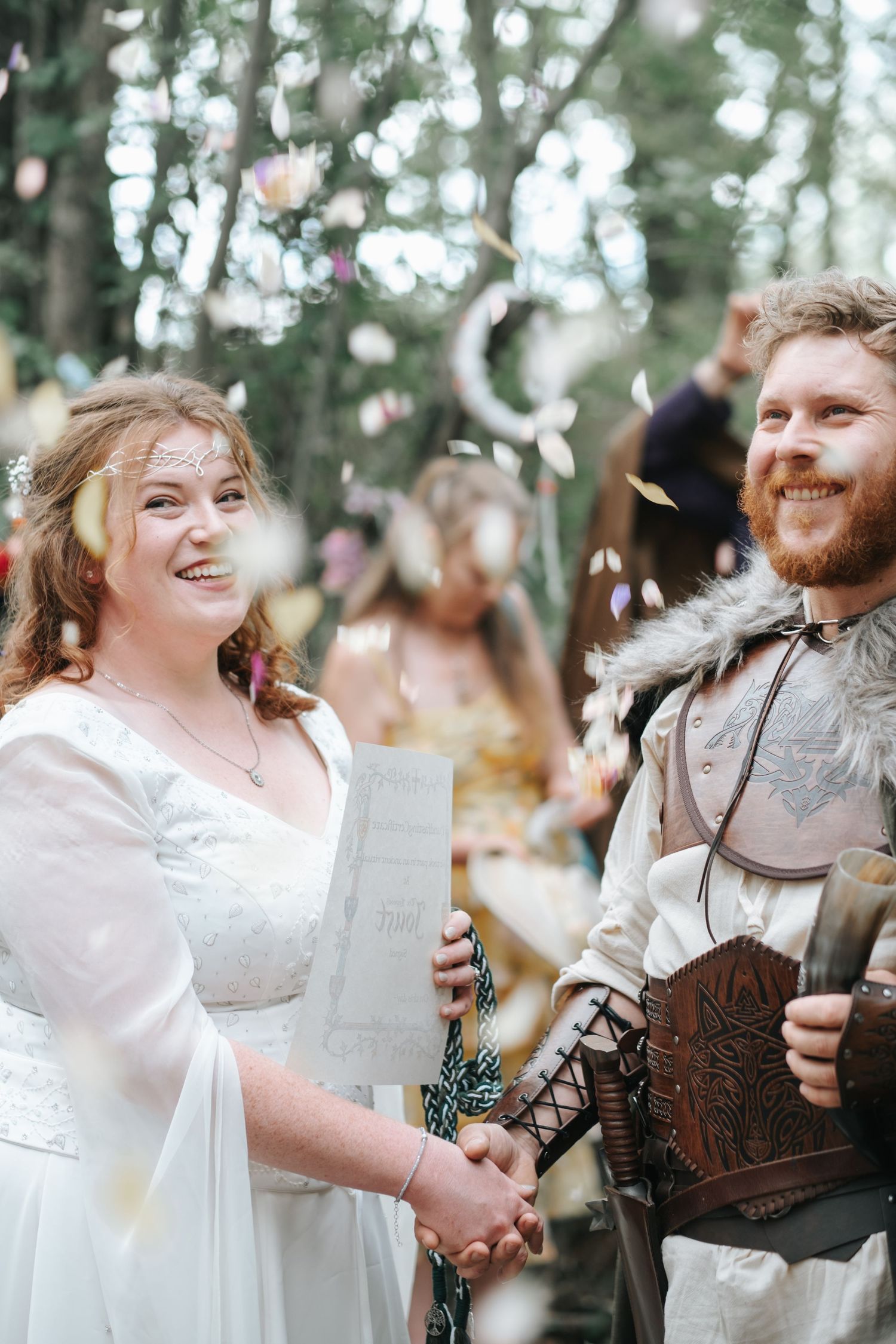 A female and male couple in medieval dress hold hands as confetti falls around them.
