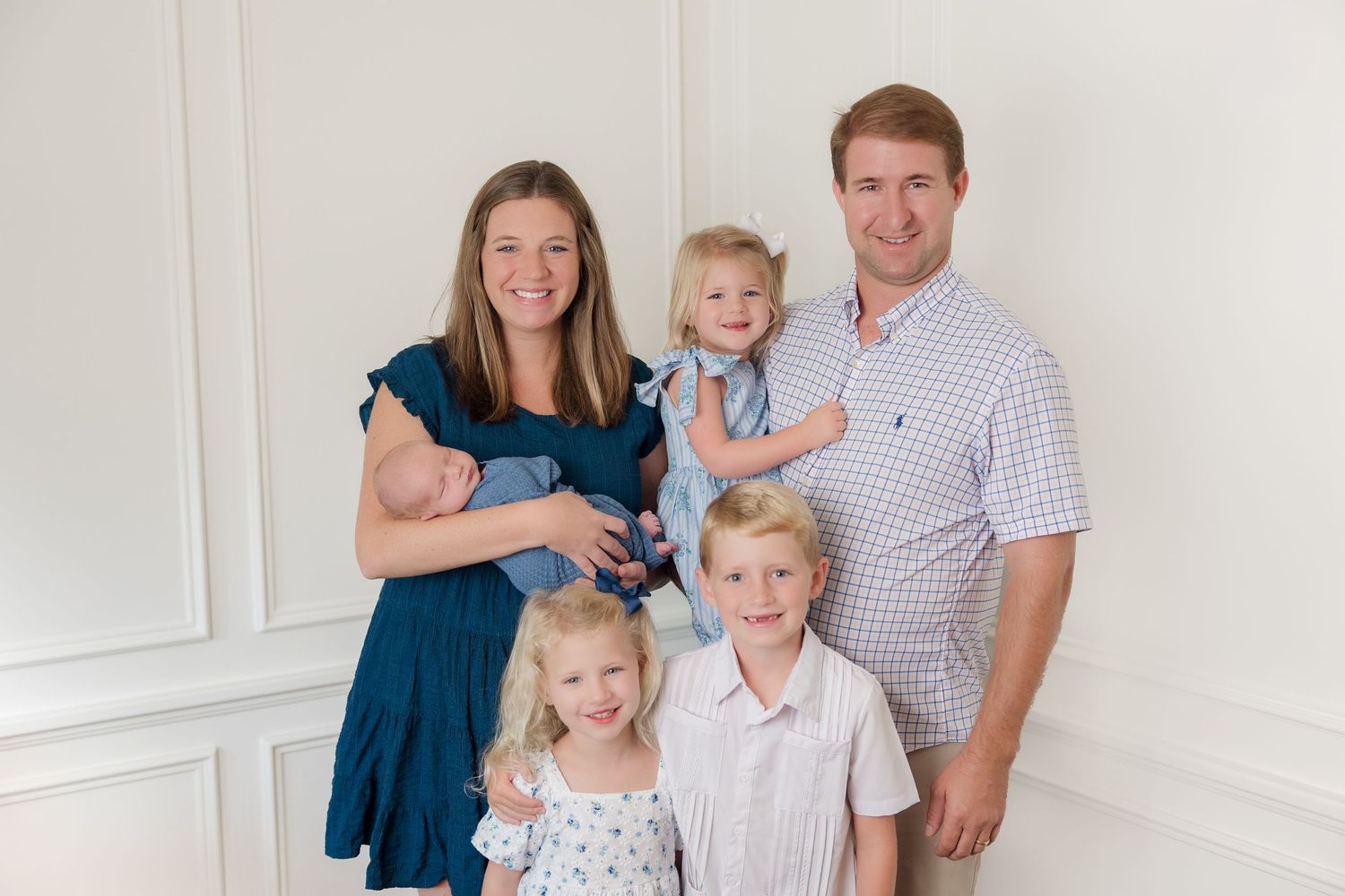 Family of five dressed in coordinating blue and white outfits posing for a formal portrait against a light background.