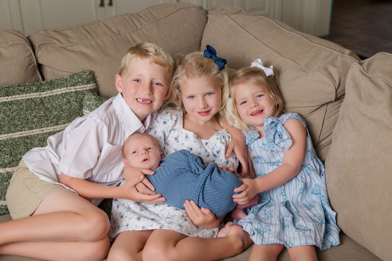 Several children wearing blue and white outfits snuggle together on a light-colored couch.