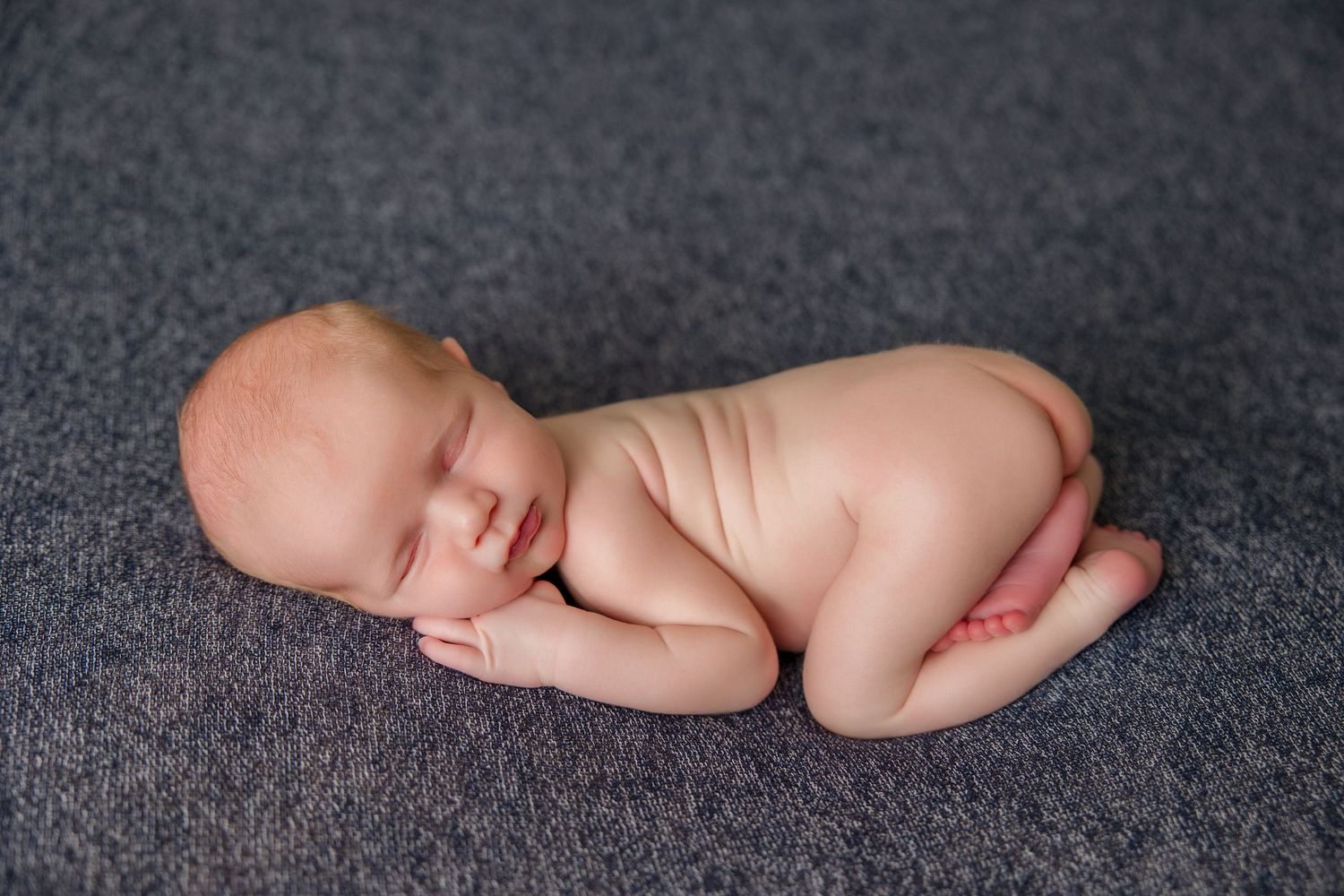 A newborn baby sleeping peacefully on a dark grey textured surface.