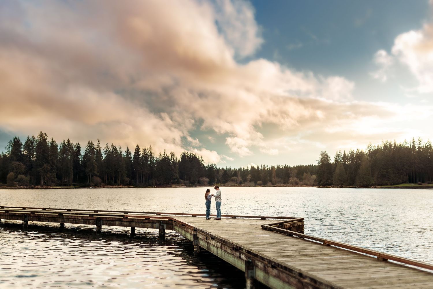 Wooden dock stretches over calm lake waters during dramatic sunset.