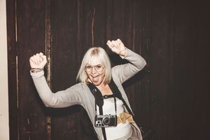 A person in a white outfit with glasses dancing joyfully against a dark background.