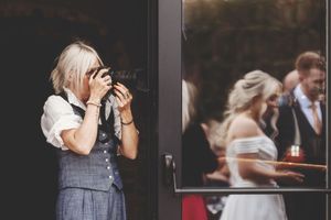 Wedding photographer takes photos through doorway while couple poses in background.