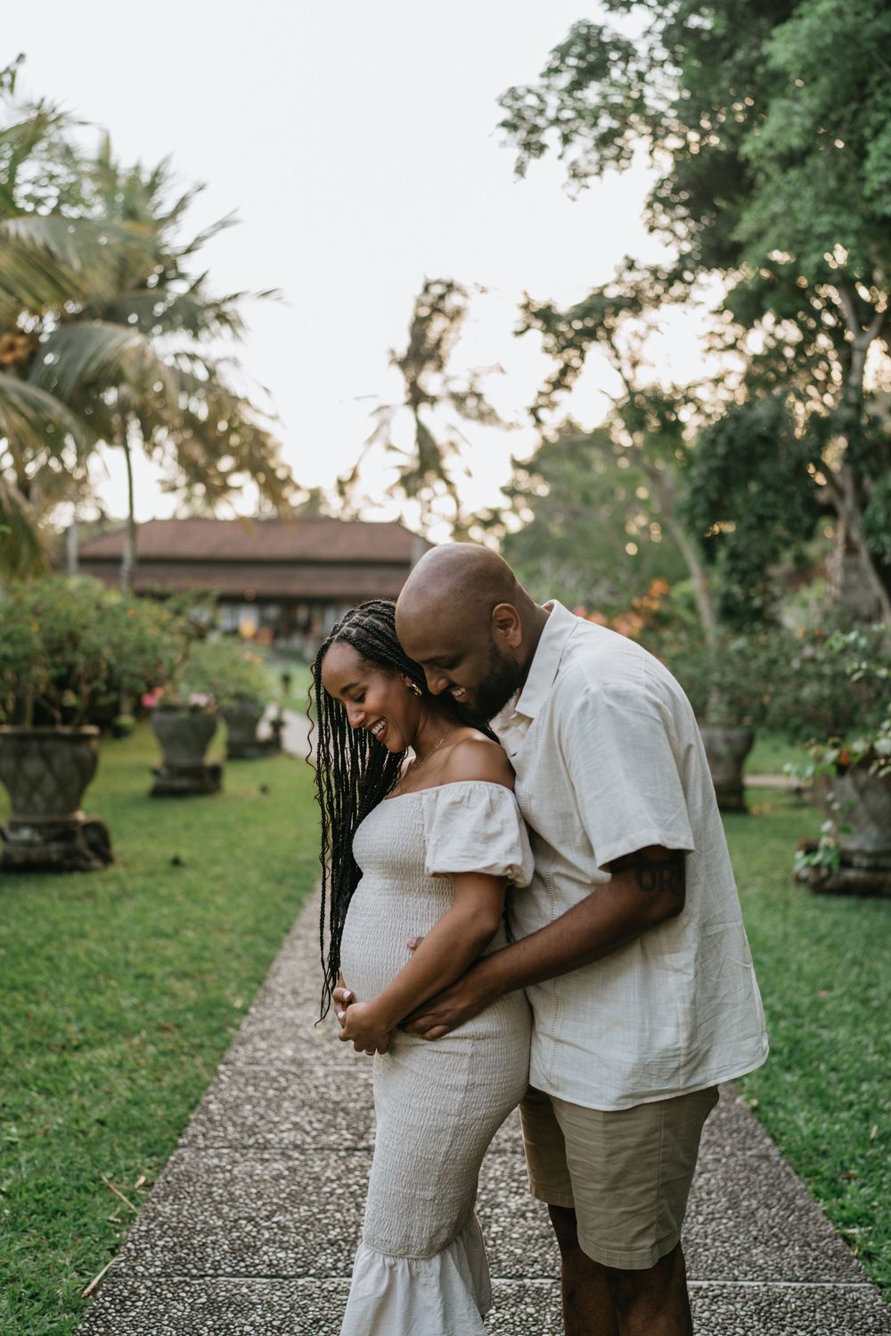 A romantic couple embraces on a garden path surrounded by lush tropical landscaping.
