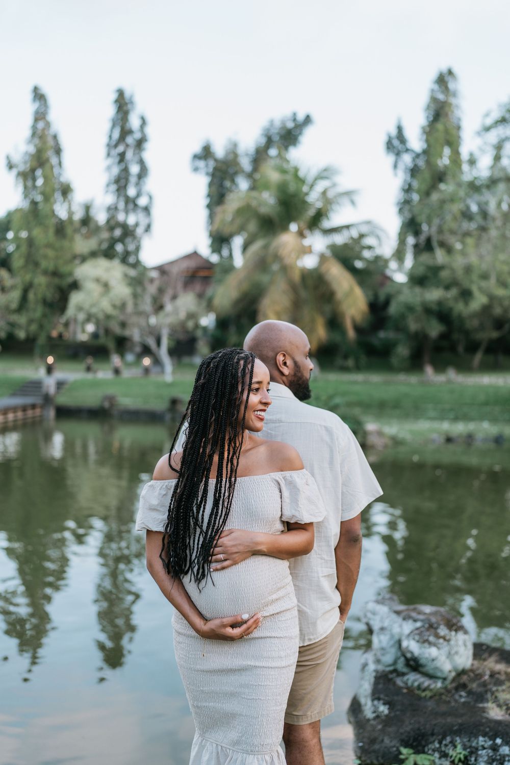 Romantic couple embraces by a serene lake surrounded by palm trees during a photo session.