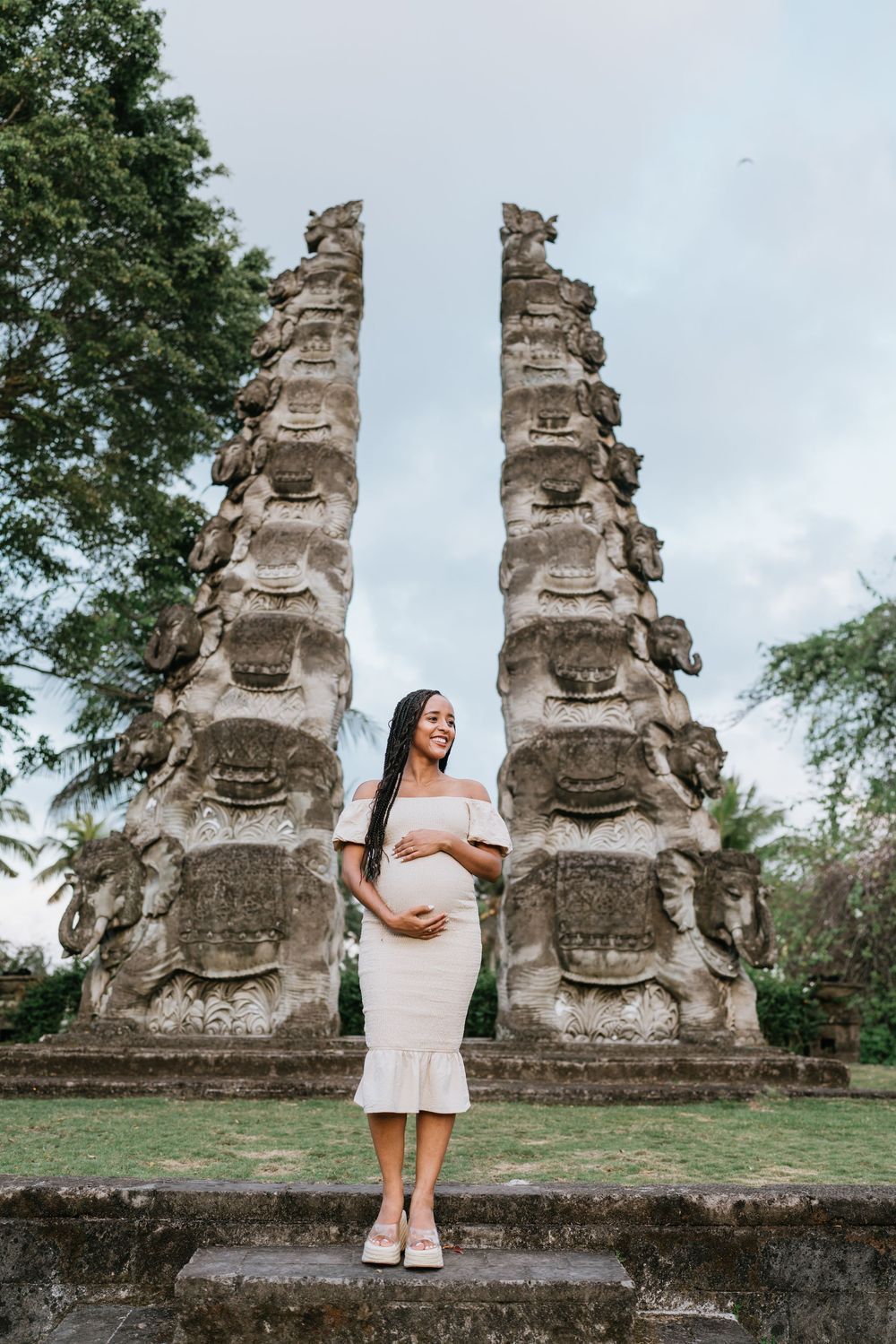 White dress against ancient stone temple statues creates elegant contrast in outdoor portrait setting.