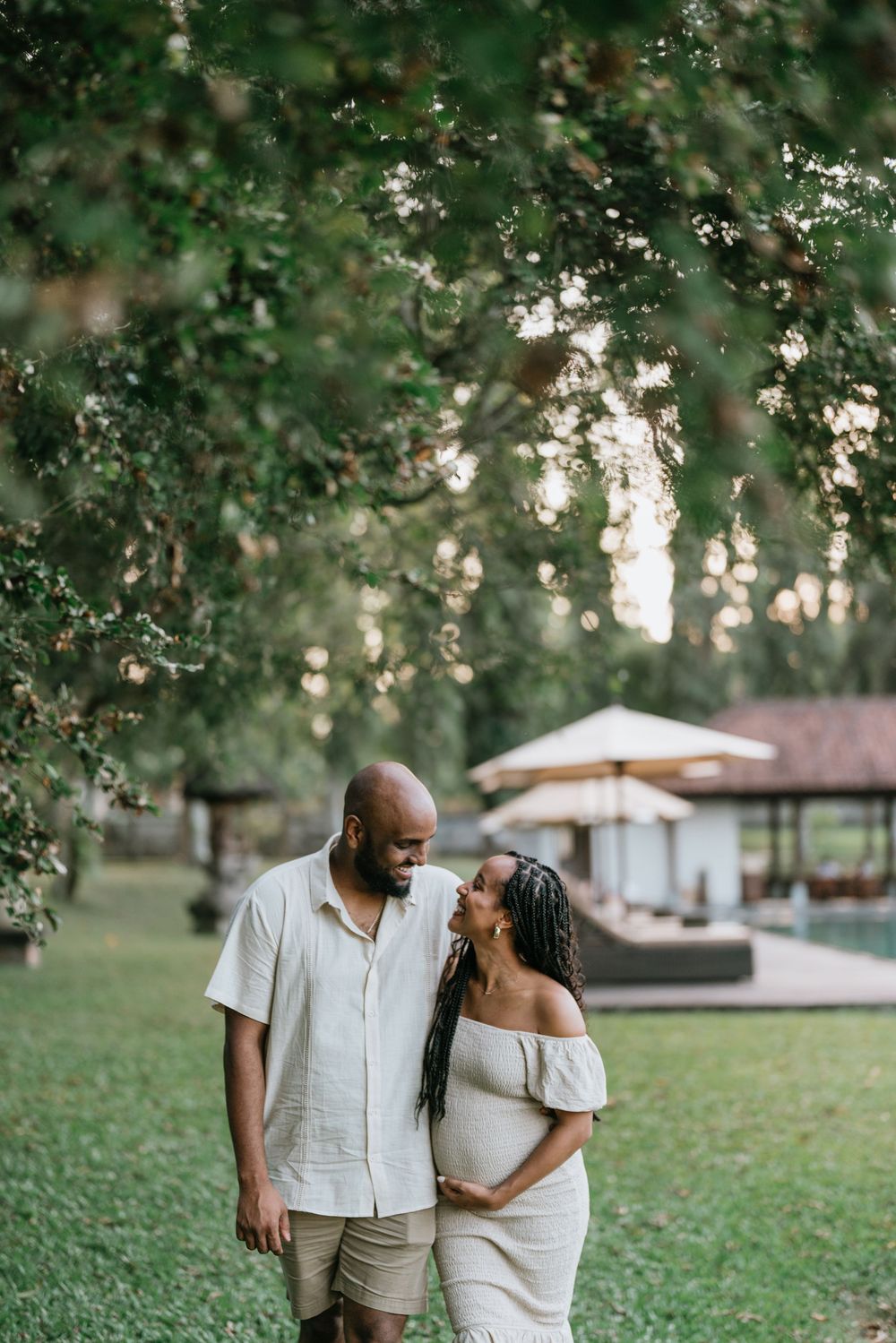Couple in coordinated white and beige outfits walk together on grassy lawn at sunset.