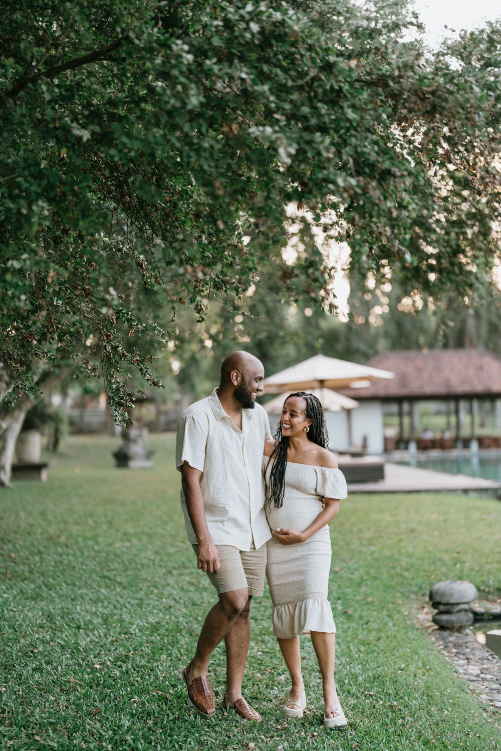 Couple shares intimate moment while walking through park with trees and building in background.