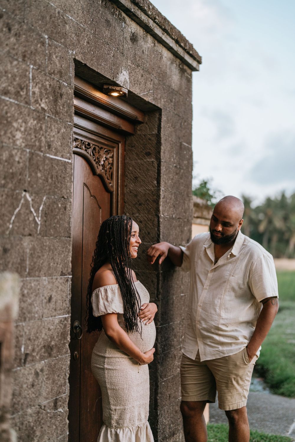 Romantic couple shares intimate moment against rustic stone wall and wooden doorway.