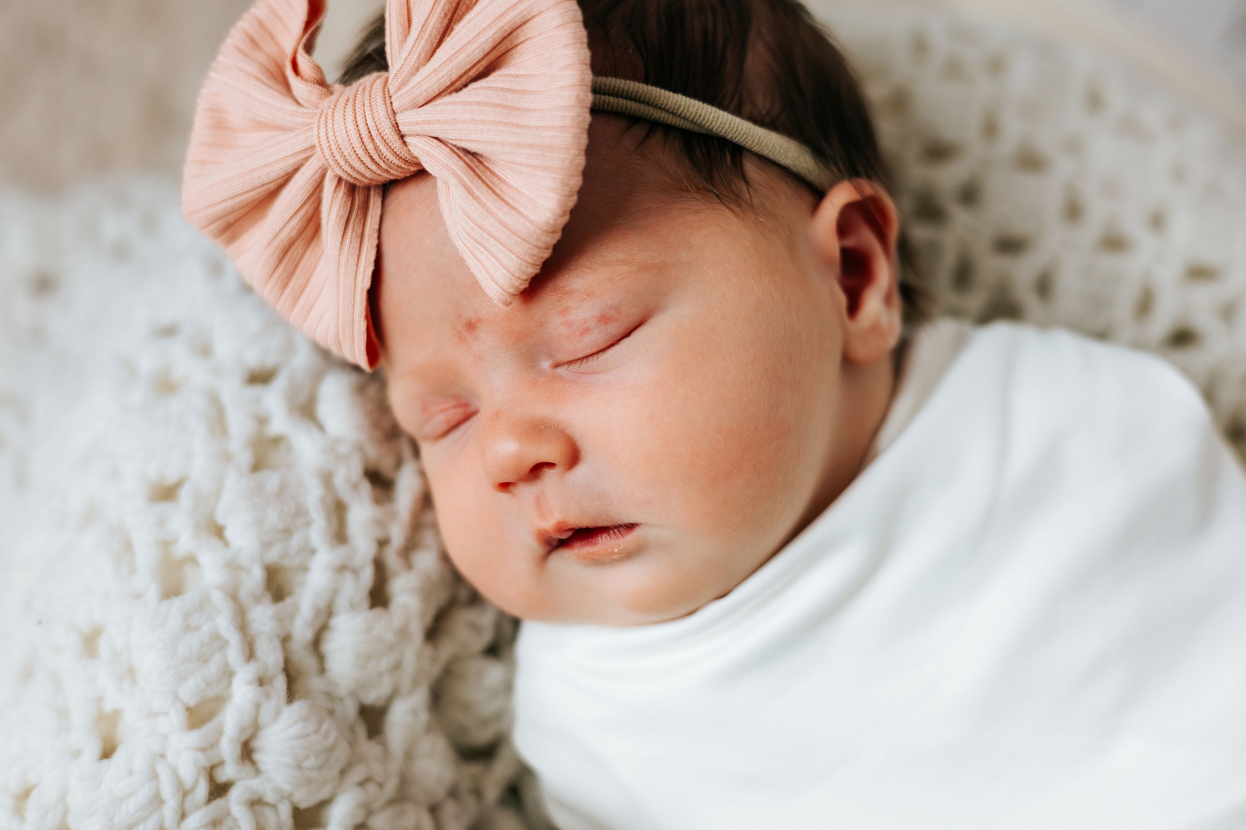 Sleeping baby wearing pink bow headband in soft natural light.