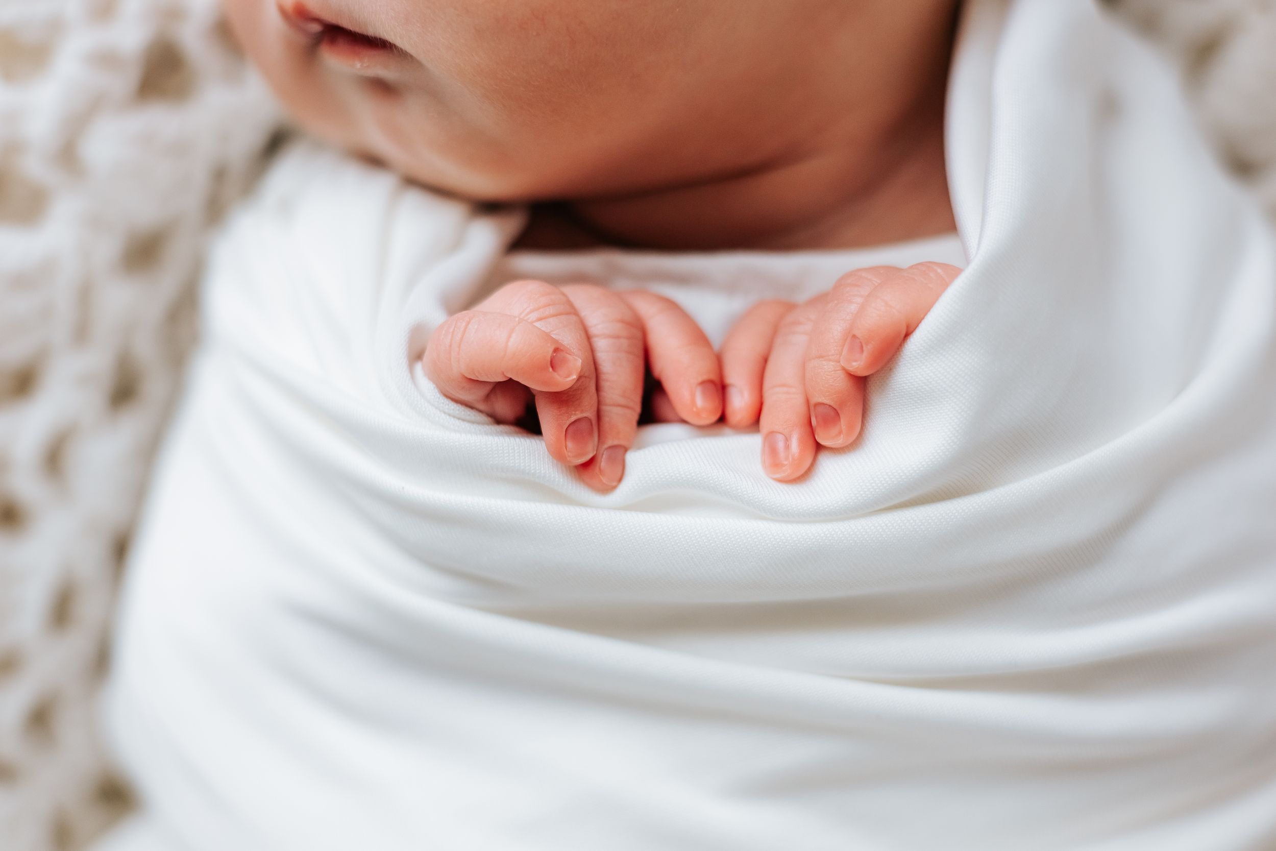 Close-up details of newborn baby wrapped in white swaddle blanket.