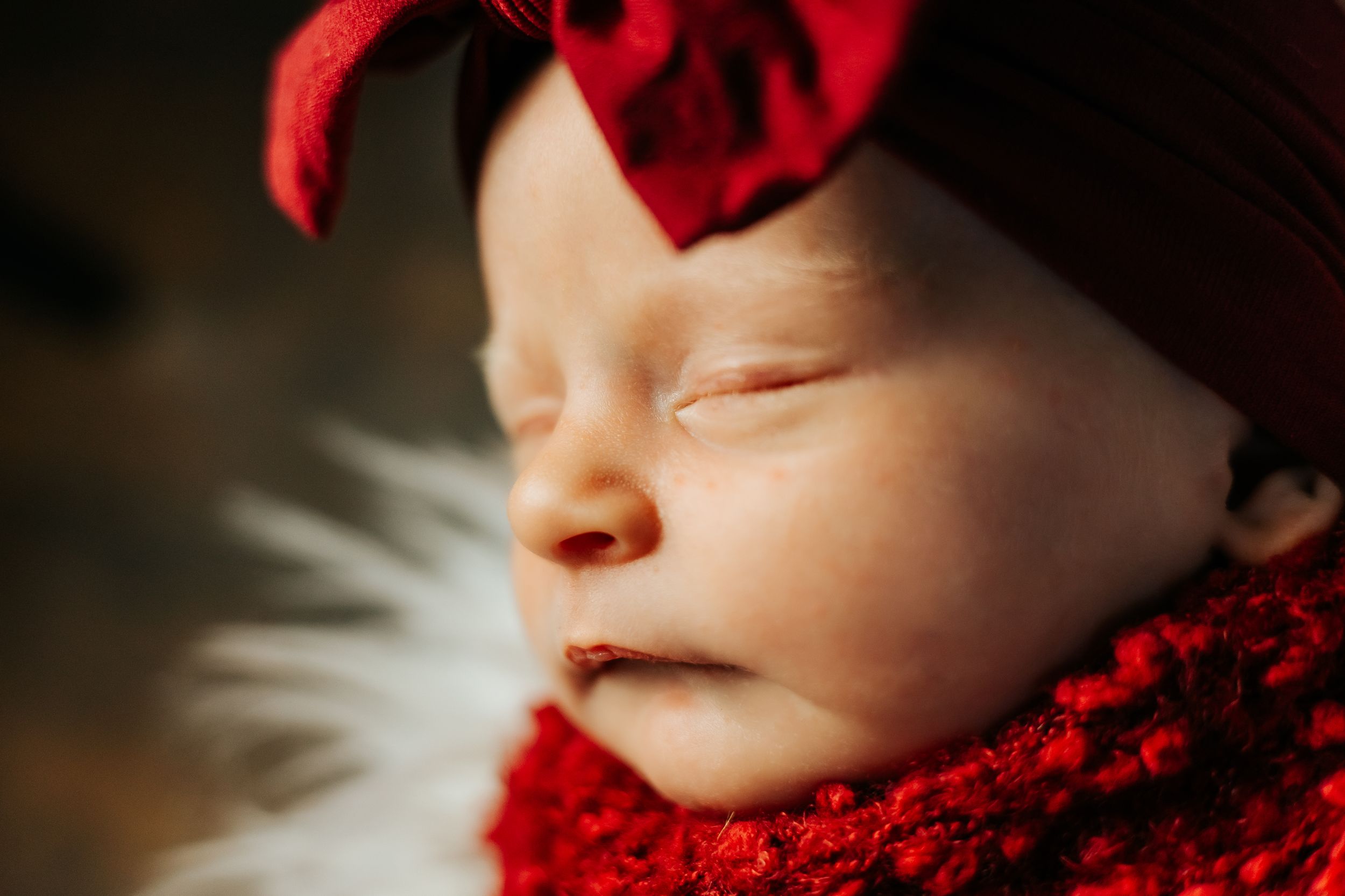 Sleeping newborn wearing red knit clothing on white textured background.