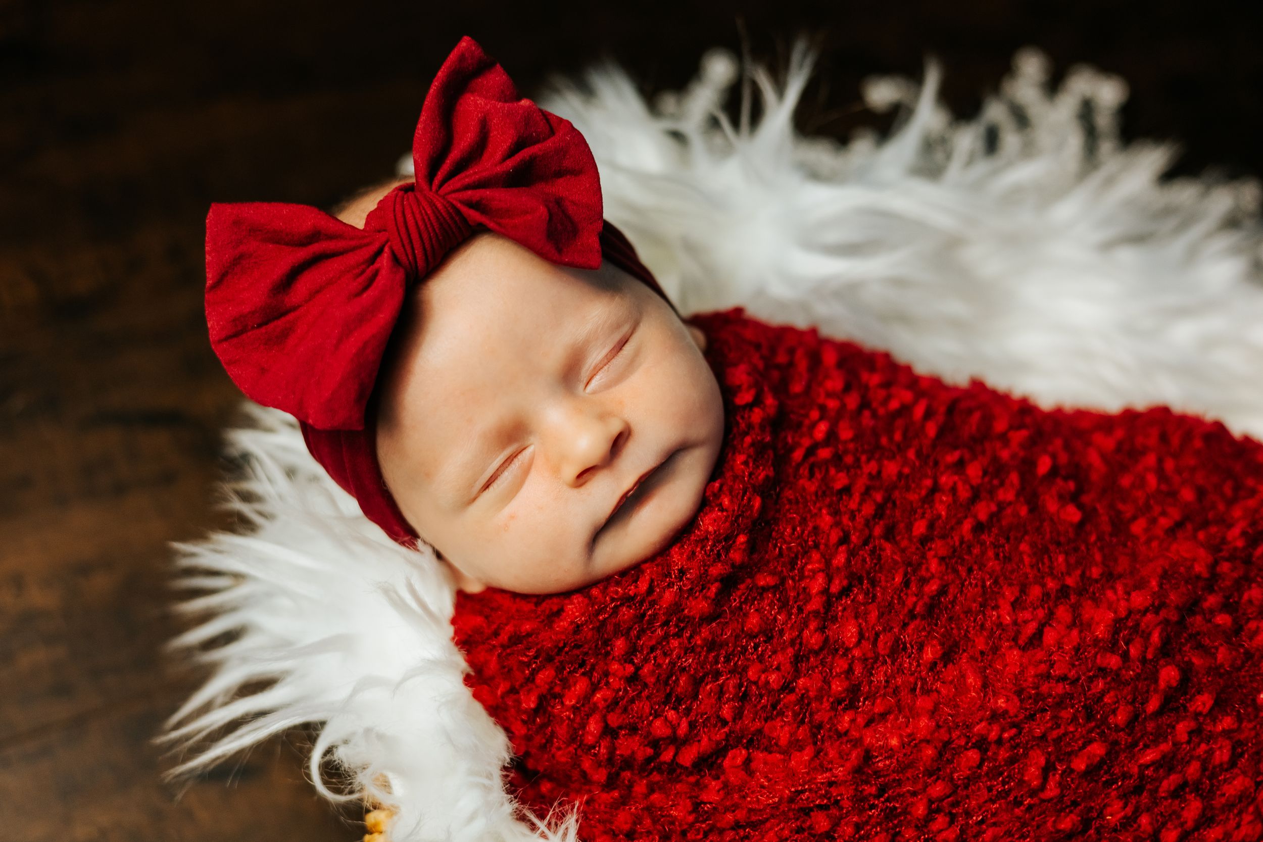 Newborn baby wrapped in red knit fabric against dark backdrop.