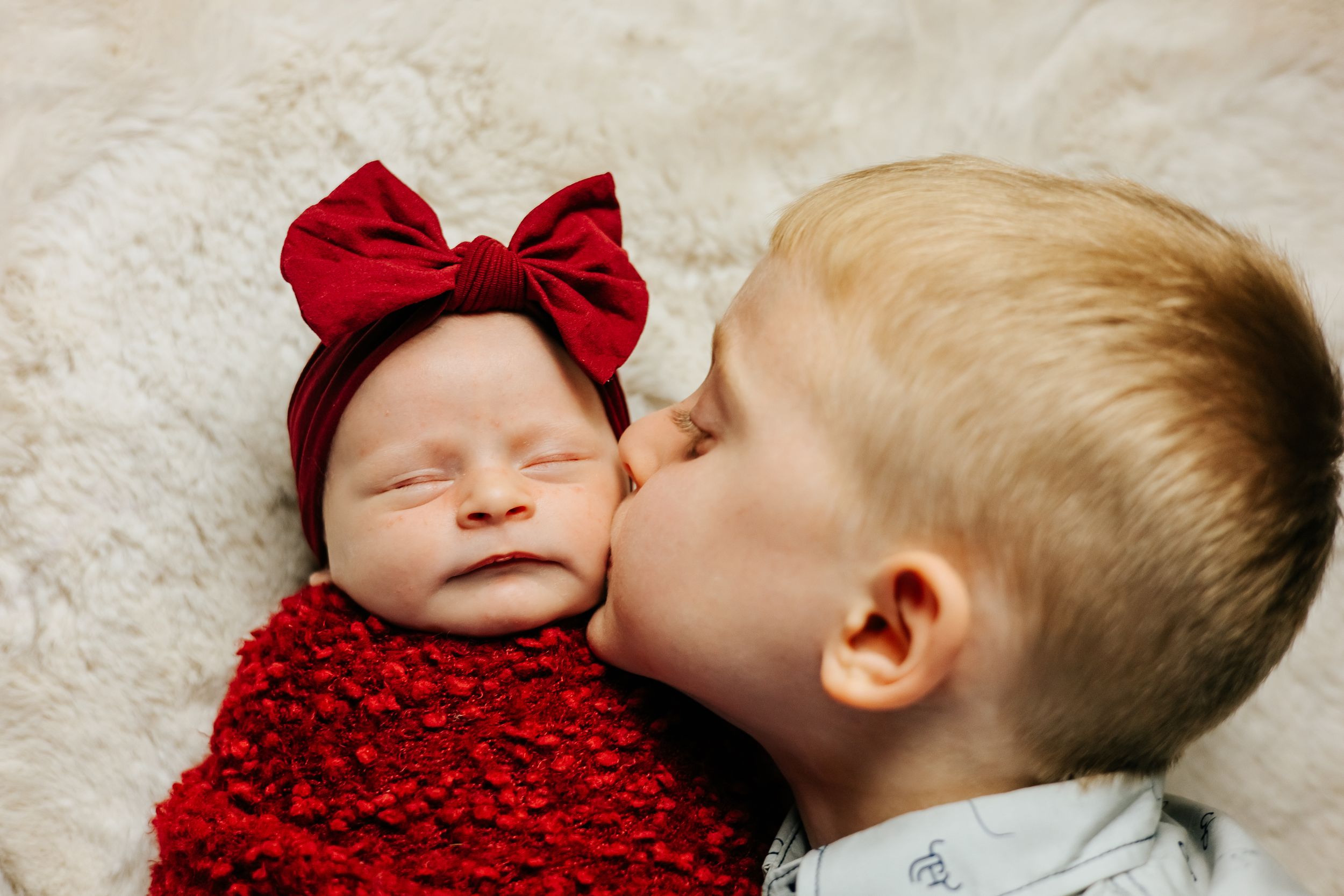 Baby wearing red bow resting on white fluffy blanket.