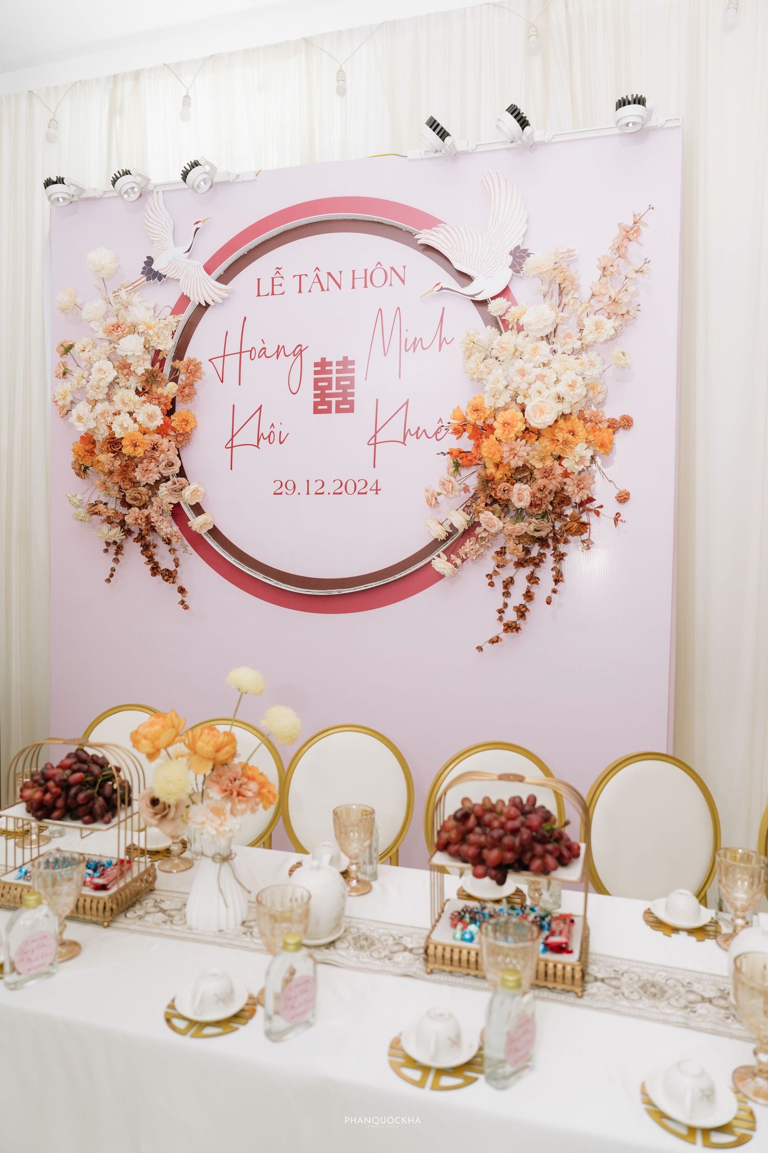 Pink and gold engagement party backdrop for Hoang Khoi and Minh Khue with floral decorations and table setup.