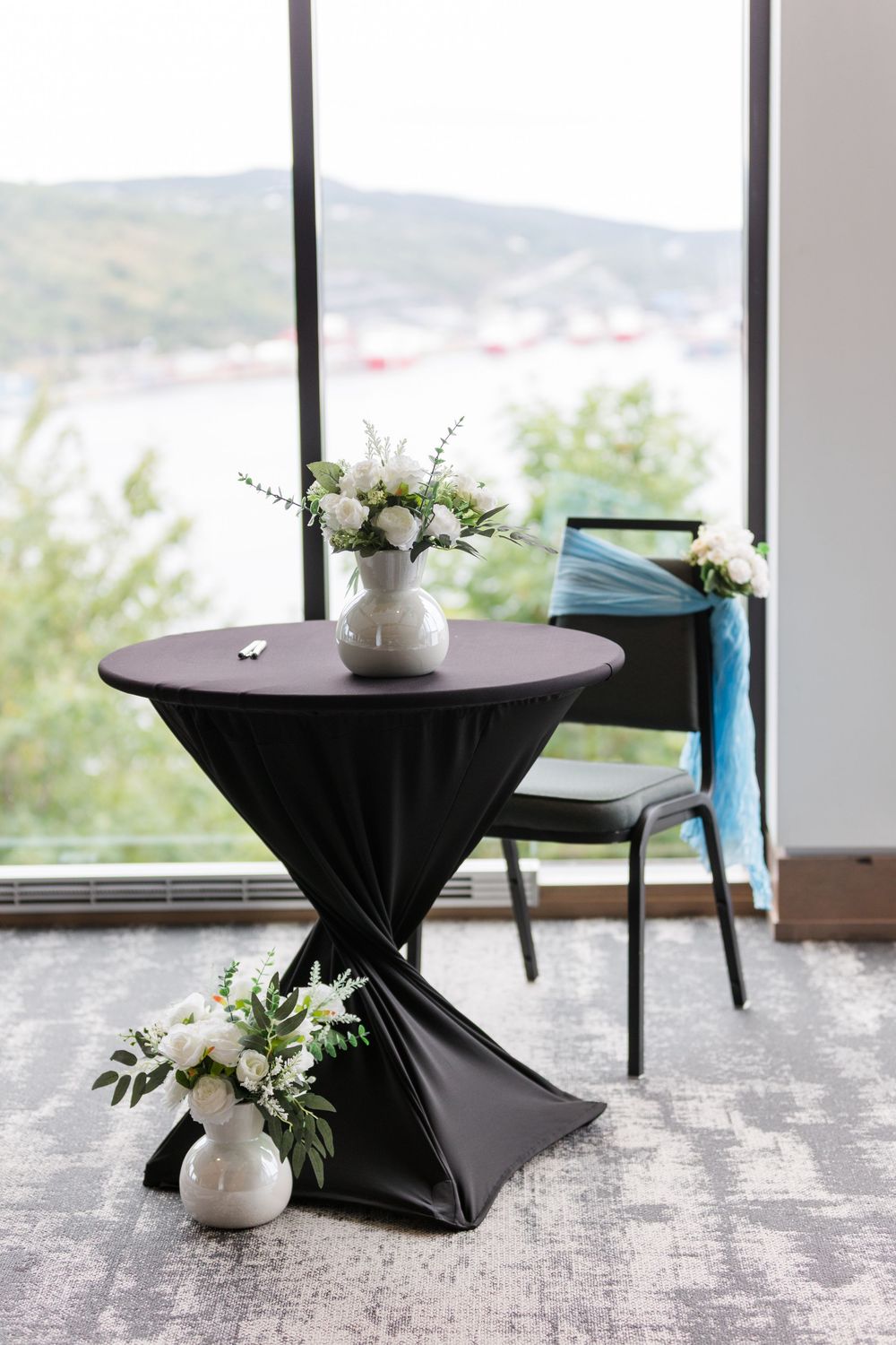 Modern geometric black pedestal tables with white floral arrangements against floor-to-ceiling windows with mountain views.