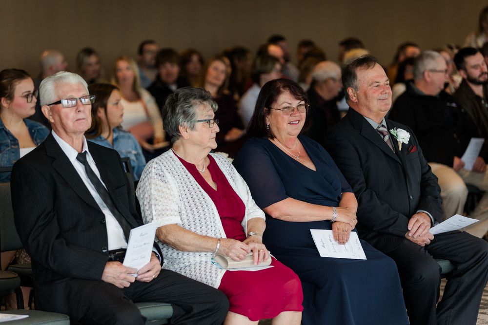 Wedding guests seated in rows watch and smile during ceremony.