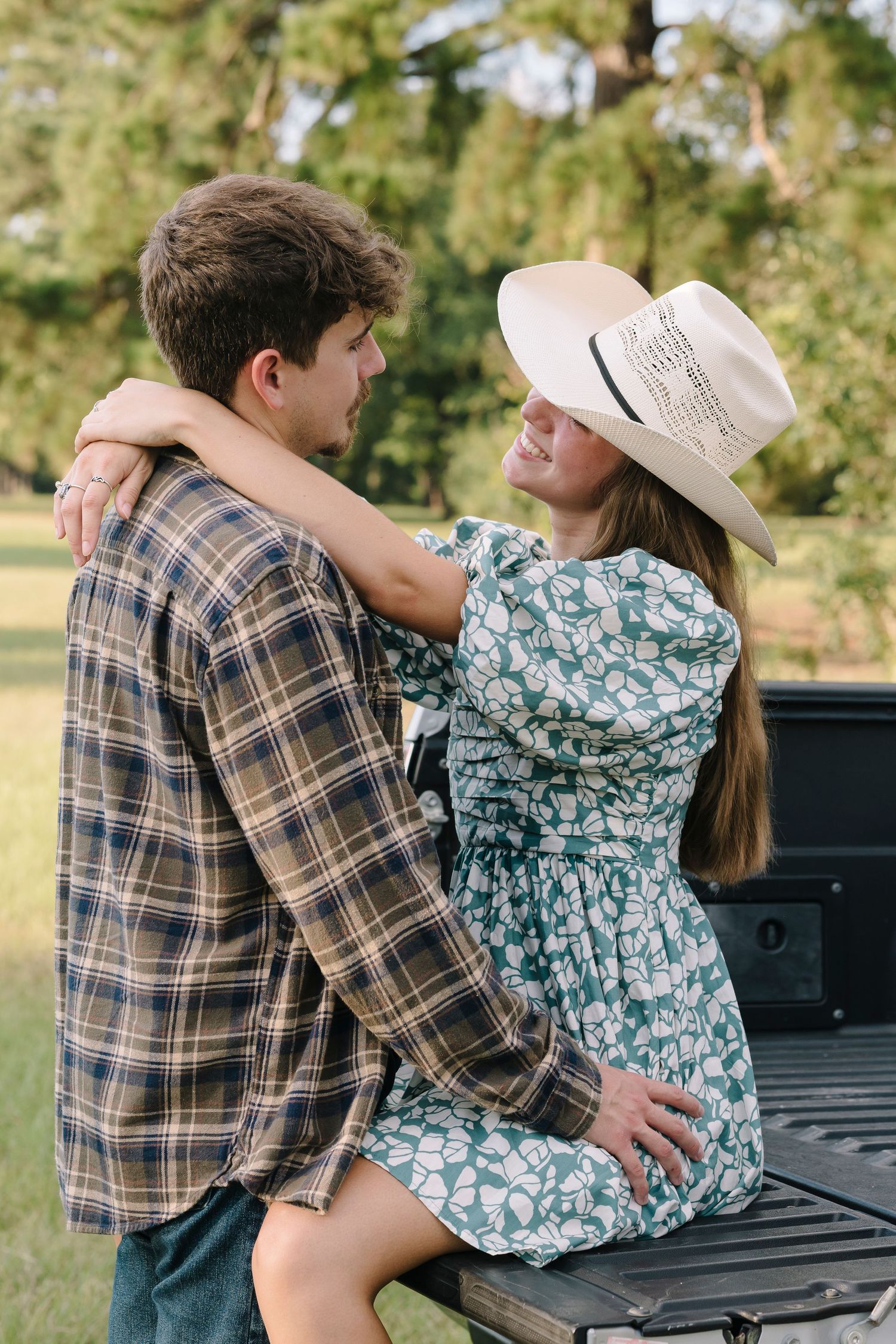 A couple in western attire shares a playful dance moment on a pickup truck bed during a sunny outdoor photoshoot.
