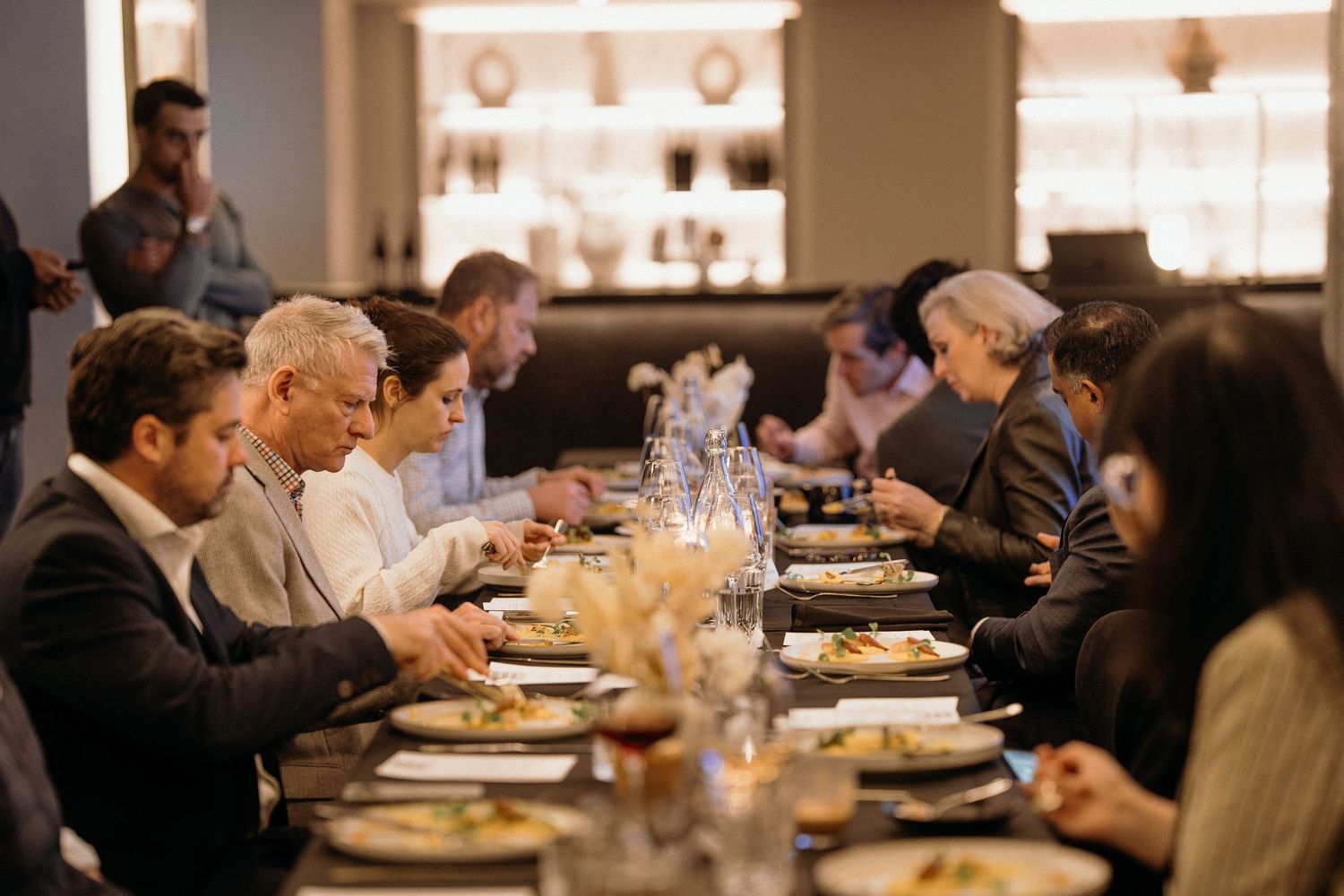 Diners seated at elegant restaurant tables enjoy an upscale dining experience in warm ambient lighting.